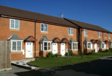 A street of small, cottage-style red brick houses against a blue sky